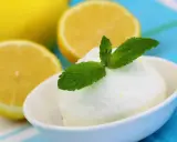 Crème glacée citron rafraîchissante, garnie de menthe fraîche, avec des citrons coupés en arrière-plan.