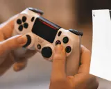 Ręce trzymające biały kontroler DualShock 4, obok konsoli PS5. Dowiedz się, jak podłączyć pada PS4 do PS5.