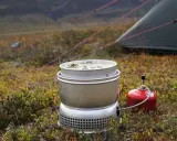 Matlagning på ett esbit kök i fjällen. En kastrull med mat värms upp bredvid ett tält.