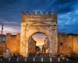 Arco d'Augusto a Rimini al tramonto, con il cielo drammatico e la folla che passeggia. Un'icona della mir fiera Rimini.
