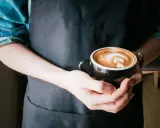 Barista hält eine Tasse mit Latte Art, die die perfekte Cortado Zubereitung zeigt.