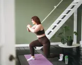 Frau macht Ausfallschritte auf einer Matte. Ihr **Crossfit zuhause**-Workout ist im vollen Gange, mit einer Leiter und einer Pflanze im Hintergrund.