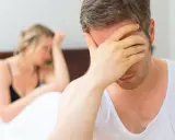 Mężczyzna w bieliźnie zakrywa twarz dłonią, kobieta w tle odwrócona.