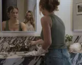 Una ragazza si pulisce il lavandino mentre un'altra la osserva riflessa nello specchio. La scena suggerisce una trama di famiglia complessa.