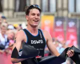 Lächelnder Athlet durchbricht die Ziellinie beim Triathlon Sprint, jubelnd mit schwarzem Band.