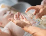 En hand sprutar olja i en annan hand, redo att smörja en bebis. Kanske för att lindra skorv bebis.