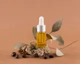 Flacon d'huile dorée, posé sur une pierre avec des graines et des feuilles séchées. Un élixir naturel pour des cheveux éclatants, comme l'huile de ricin cheveux.