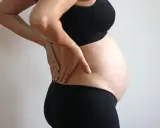 Gravid kvinna med handen på ryggen, upplever ont i ljumsken.