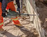 Trabajador con martillo neumático realiza demolición manual de muro de hormigón.