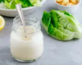 Un pot de vrai sauce césar crémeuse, avec une feuille de laitue romaine et un quartier de citron.