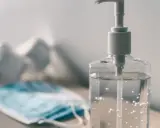 Butelka płynu do dezynfekcji i maseczka ochronna na stole.
