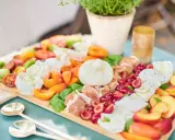Eine üppige Antipasti Platte mit Burrata, Kirschen, Pfirsichen, Tomaten und Prosciutto.