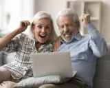 Szczęśliwi seniorzy sprawdzają na laptopie przeliczenie emerytury rocznik 1949 do 1953.