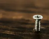 Un tornillo plateado sobre madera oscura. Para sacarlo, gira hacia la izquierda.