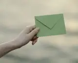 Dłoń trzyma zieloną kopertę, gotową do wysłania. Zastanawiasz się, jak podpisać kopertę? To proste!