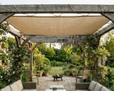 Une toile beige est tendue pour couvrir une tonnelle en bois, offrant un coin ombragé dans un jardin fleuri.