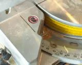 Detalle de una sierra ingletadora con marcas de ángulo para saber como medir para cortar a inglete. Se ve serrín y una advertencia de seguridad.