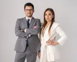 Para prawników w garniturach, mężczyzna w szarym, kobieta w białym, na jasnym tle.