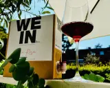 Ein Glas Rotwein steht neben einem Karton mit der Aufschrift "WE IN Box". Der Wein im Karton ist eine praktische Alternative zur Flasche.