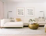 En ljus soffgrupp med en mönstrad matta och ett runt soffbord i mässing. Två grafiska tavlor hänger på väggen.