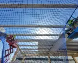 Trabajadores en plataformas elevadoras instalan una red de protección colectiva sobre una estructura en construcción, garantizando la seguridad.