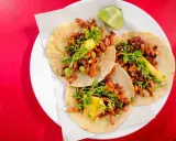 Tres deliciosos tacos al pastor, con cilantro, piña y un toque de limón, listos para disfrutar.