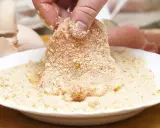 Fleisch wird in Paniermehl gewendet. Eine Hand hält das Stück, um es perfekt panieren ohne Ei zu machen.