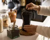 Manos preparando un café con alcohol en cafetera italiana. Hay frascos con avena y café molido.