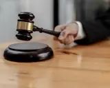 Mano che impugna un martelletto da giudice, pronto a battere sul ceppo. Il suo significato, il g.u.p., è un momento cruciale.