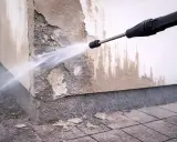 Hochdruckreiniger sprüht Wasser auf eine beschädigte Hauswand, um die Fassade zu reinigen.