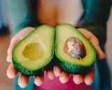 Zwei Hälften einer Avocado werden in Händen gehalten. Eine Hälfte hat den Kern, die andere ist leer. Perfekt, um die Avocado reifen zu lassen.