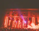 Folla in delirio al **mood festival**, illuminata da luci al neon rosse e fumo denso. La scena è un'esplosione di energia.