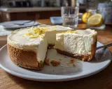En krämig, fryst cheesecake med citronskal på toppen står på ett fat. En bit är bortskuren.