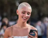 Junge Frau mit buzz cut blond, lächelnd und auf ihr Handy schauend.
