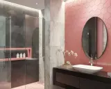 Bagno moderno con pareti rosa a nido d'ape, doccia in vetro e marmo. Un lavabo ovale su mobile nero e specchio rotondo completano le idee bagno rosa.