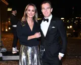 A couple in formal attire poses at night with a blurred city background.