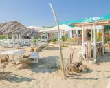 Un angolo di cervia strand con tavoli, sedie e ombrelloni di paglia, pronto ad accogliere i bagnanti.