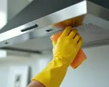 Ręka w żółtej rękawiczce czyści okap ze stali nierdzewnej pomarańczową ściereczką. Dowiedz się, czym wyczyścić okap ze stali nierdzewnej, by lśnił jak nowy.