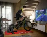 Mężczyzna ćwiczy na rowerze stacjonarnym, korzystając z aplikacji do trenażera, która wyświetla wirtualną trasę na dużym ekranie telewizora.