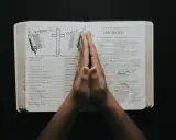 Dłonie złożone w modlitwie nad otwartą Biblią, z tekstami do modlitwy uwielbienia.