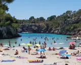 En livlig strand vid Cala Pi, med folk som badar i det turkosa vattnet och solar på sanden under parasoller.