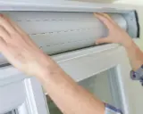 Mains ajustant un volet roulant blanc. Guidez-vous pour savoir comment réparer un volet roulant.