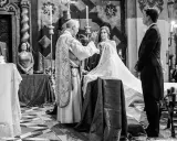 Sacerdote bendice a la pareja durante el rito de la velación. Novia con velo, novio de etiqueta, invitados y altar en iglesia.