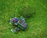 Un homme est assis sur un tracteur tondeuse, prêt à passer la tondeuse le dimanche. L'herbe est d'un vert éclatant.