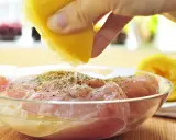 Préparation de la meilleure marinade poulet : un citron est pressé sur des morceaux de poulet assaisonnés dans un bol en verre.