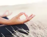 En hand i mudra-position under aum meditation, omgiven av torrt gräs.