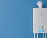 Nowy, biały piec gazowy na niebieskiej ścianie. Dowiedz się, jak wyłączyć piec gazowy na lato, aby oszczędzać energię.