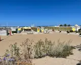 Spiaggia di Riccione con cabine gialle e blu, tavoli da ping pong e bambini in bicicletta al Bagno 19.