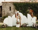 Novios besándose frente a un photocall moderno con arcos blancos y flores. ¡Ideas photocall boda únicas!