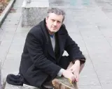 Uomo con cappotto nero seduto all'aperto, ricorda le atmosfere dei rocco schiavone libri.